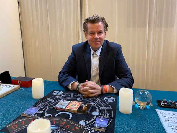 Psychic reader in Spain sitting at able with tarot cards and other fortune equipment smiling to camera | Altus Entertainment